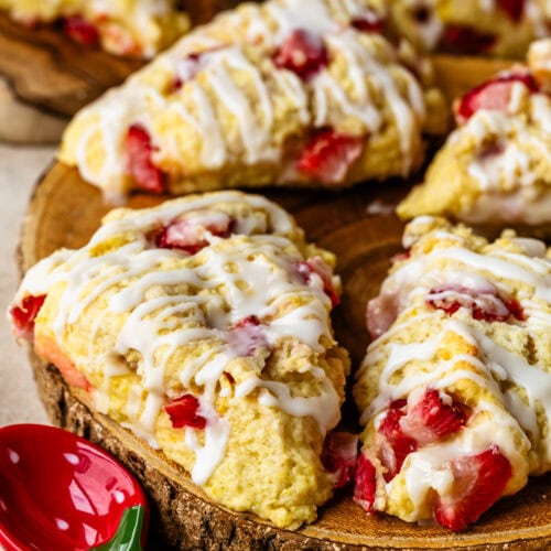 Strawberry scones with lemon glaze stacked on a wooden board.
