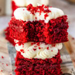 Red velvet brownied stacked on top of eachother with cream cheese frosting and red velvet crumbs, showing a moist and fudgy interior.