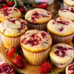 Strawberry cream cheese muffins with a golden top and visible strawberry swirls, arranged on a wooden board with fresh strawberries.