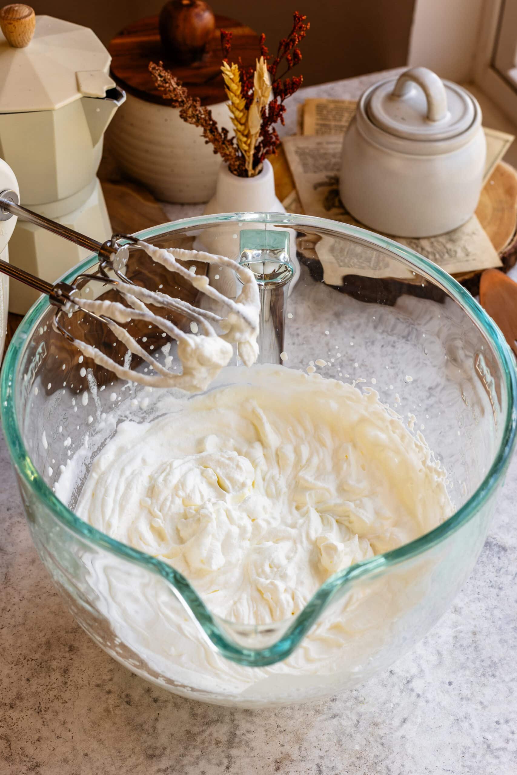 Creamy whipped topping in a glass bowl with mixer attachment, perfect for pies or toppings.