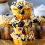 Blueberry muffins with a crumb topping stacked on a wooden board.