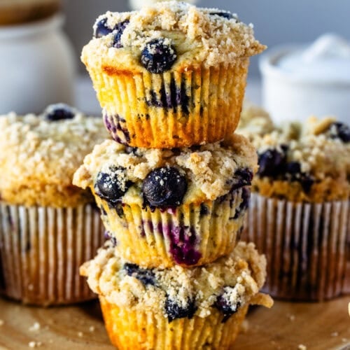 Blueberry muffins with a crumb topping stacked on a wooden board.