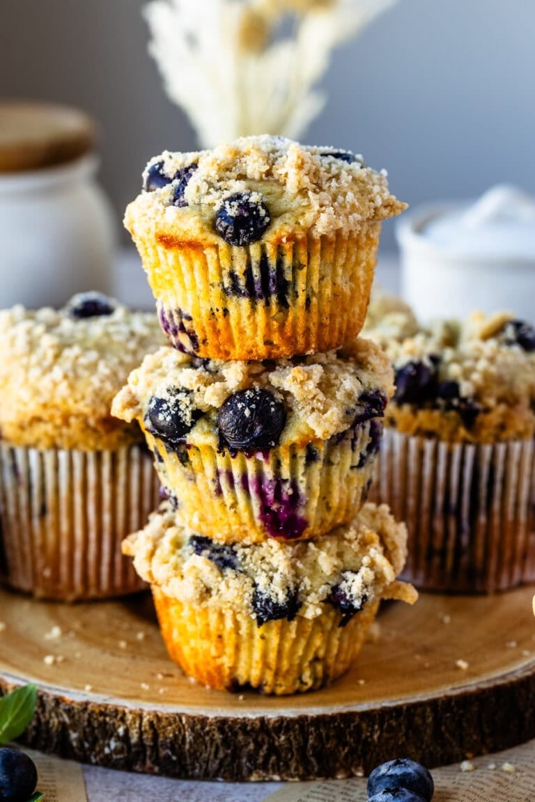 Blueberry muffins with a crumb topping stacked on a wooden board.