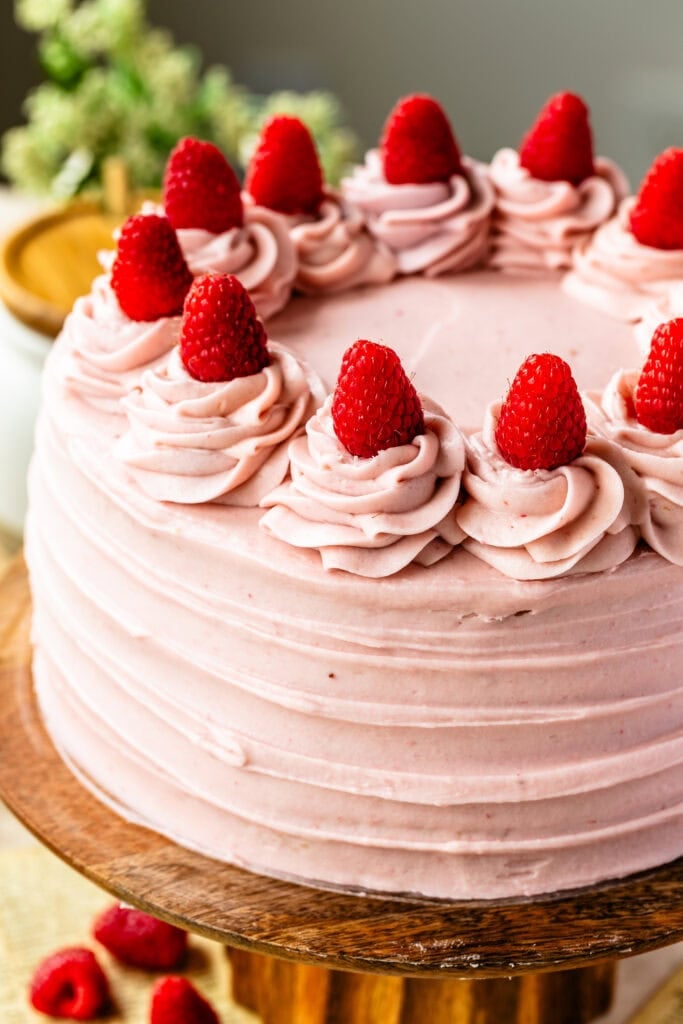 A full, delicately frosted Raspberry Cake topped with fresh strawberries on a wooden cake stand.