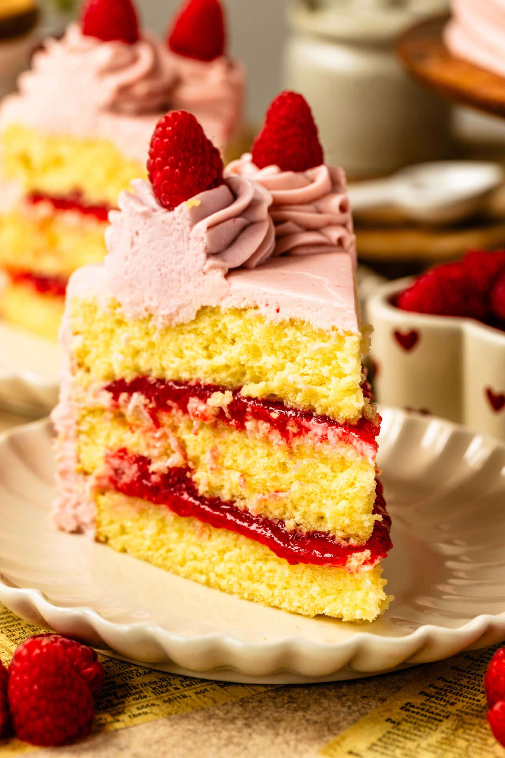 A slice of raspberry cake on a white scalloped plate.