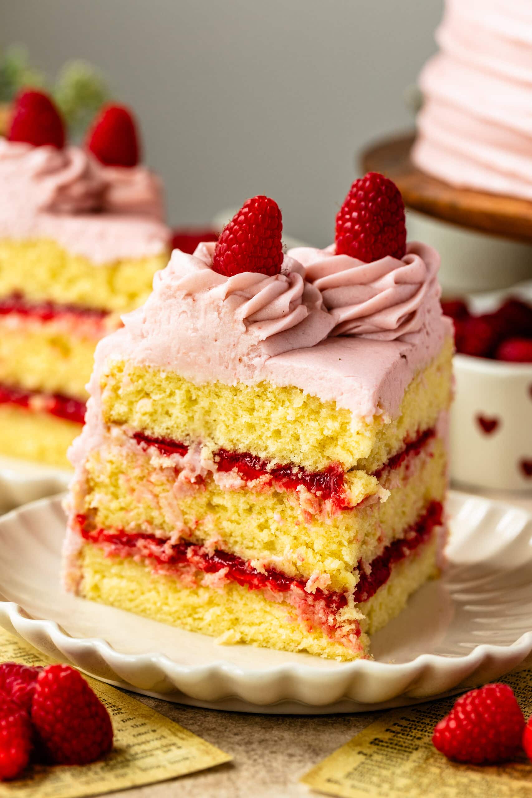 A slice of raspberry cake on a white scalloped plate.