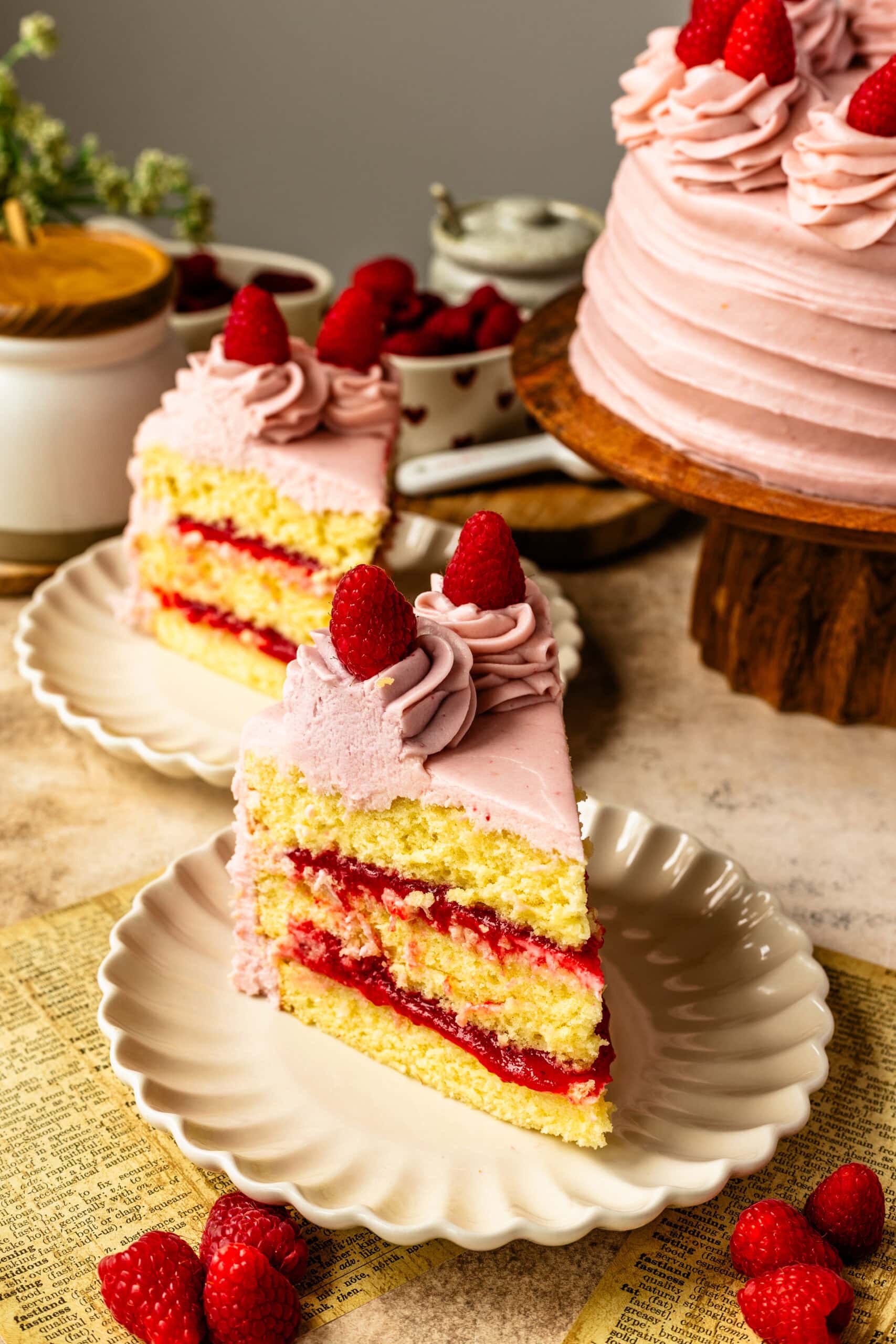 A few slices of Raspberry Cake on white scalloped plates showing the vanilla layers and jam filling.