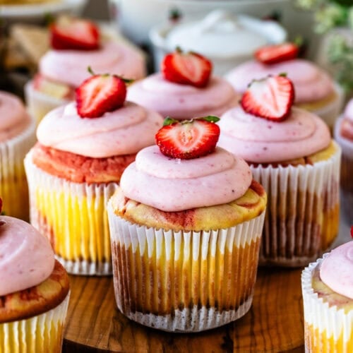 Freshly baked and decorated Strawberry Cheesecake Cupcakes on a wooden display board.