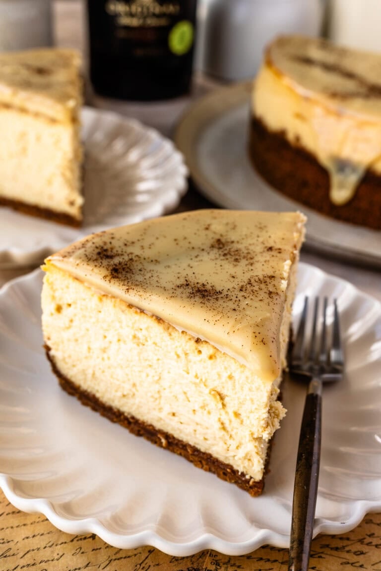 A freshly cut slice of Bailey's Cheesecake set atop a white scalloped plate and ready to be eaten.