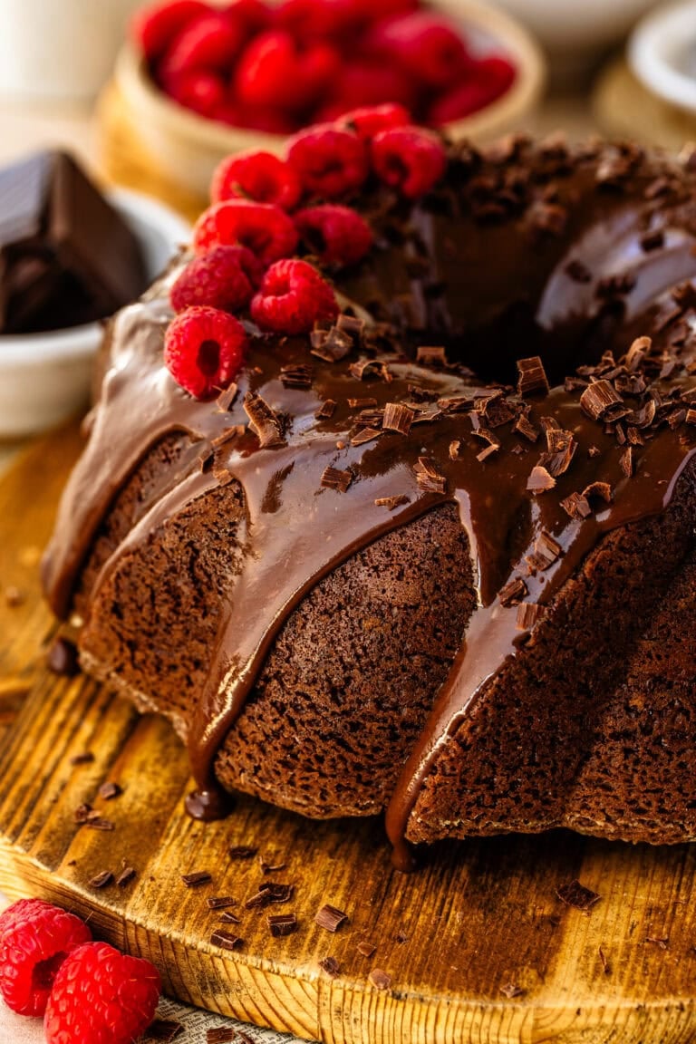 A full size Chocolate Raspberry Cheesecake Bundt Cake on a wooden board decorated with chocolate curls and fresh raspberries.