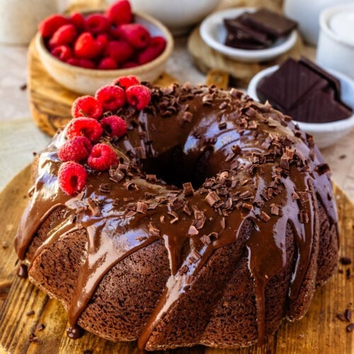 A full size Chocolate Raspberry Cheesecake Bundt Cake on a wooden board decorated with chocolate curls and fresh raspberries.