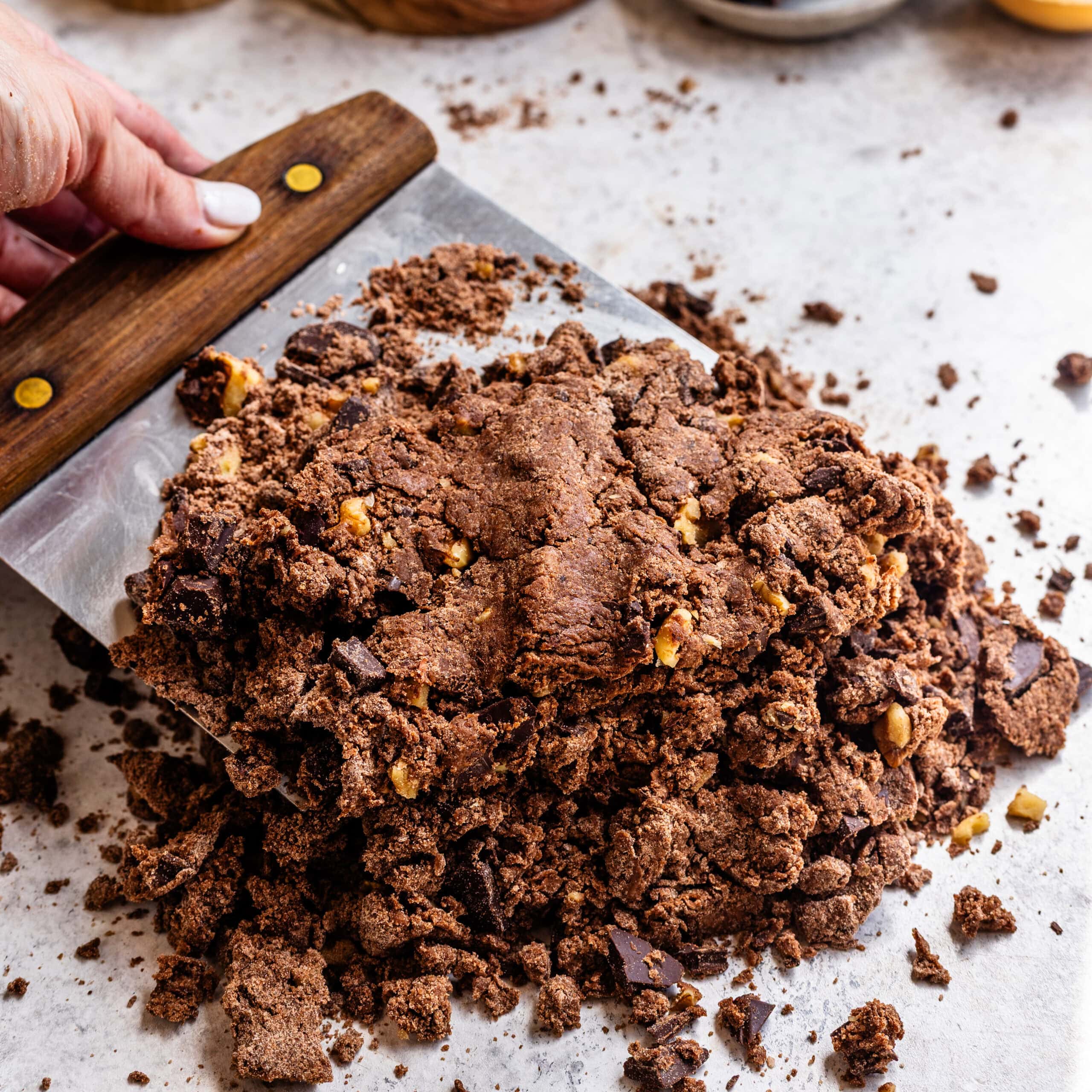 A crumbly scone dough on a kitchen work surface being mixed with a bench scraper.