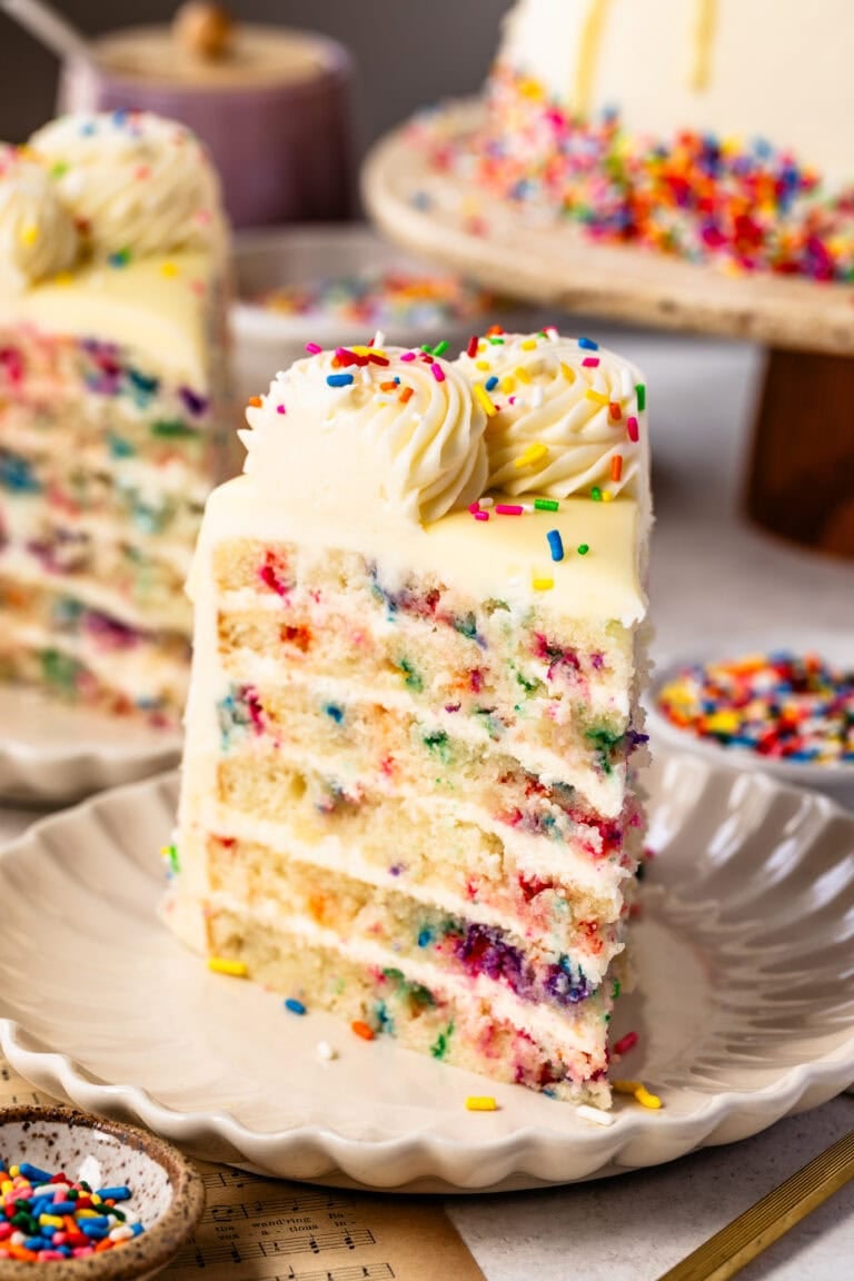 A slice of beautifully layered funfetti cake filled with sprinkles and frosted with cream cheese frosting.