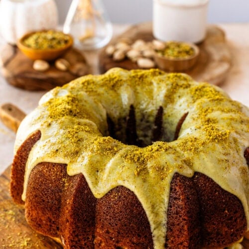A beautiful golden brown Pistachio Bundt Cake with Pistachio Ganache on a wooden serving board.