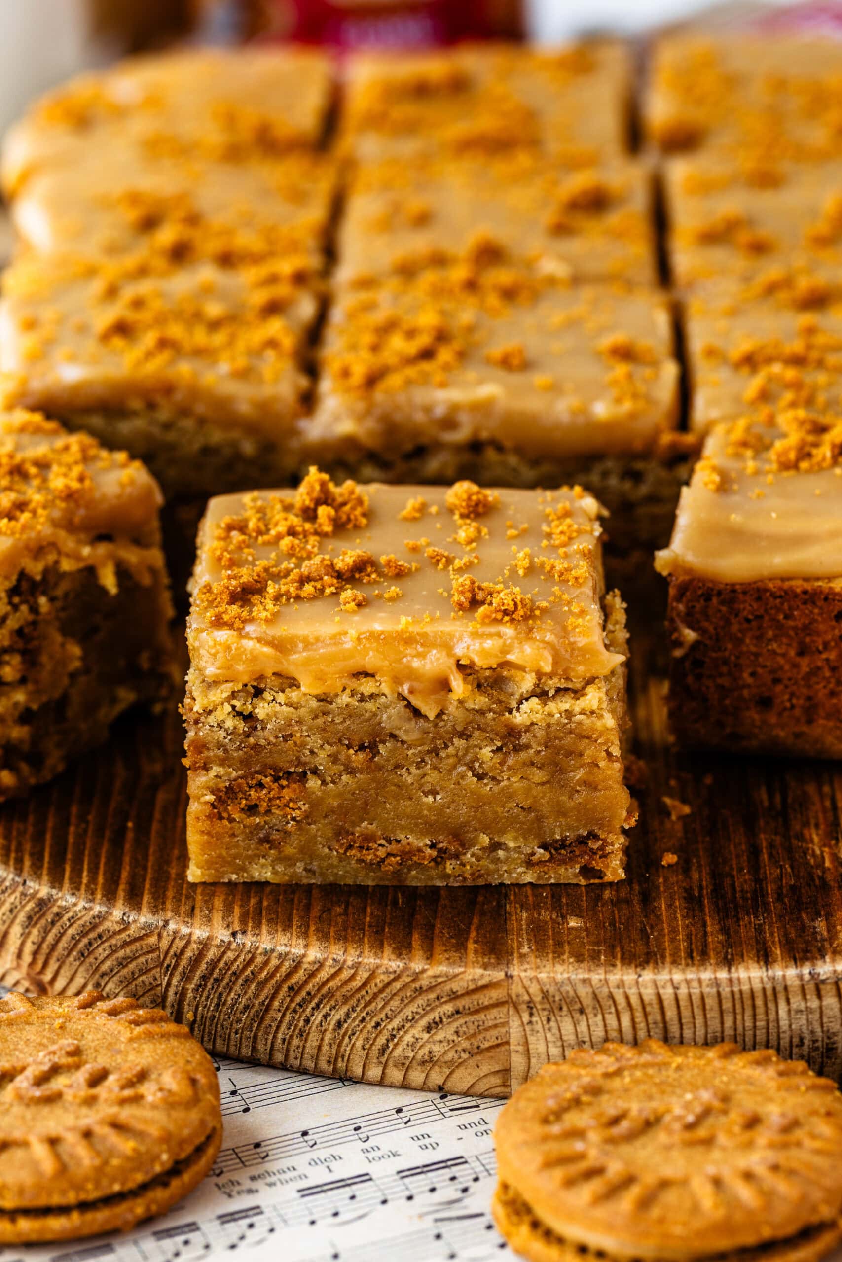 Biscoff blondies cut into squares with a thick layer of Biscoff white chocolate ganache on top, sprinkled with cookie crumbs, with one Biscoff blondie in the foreground.