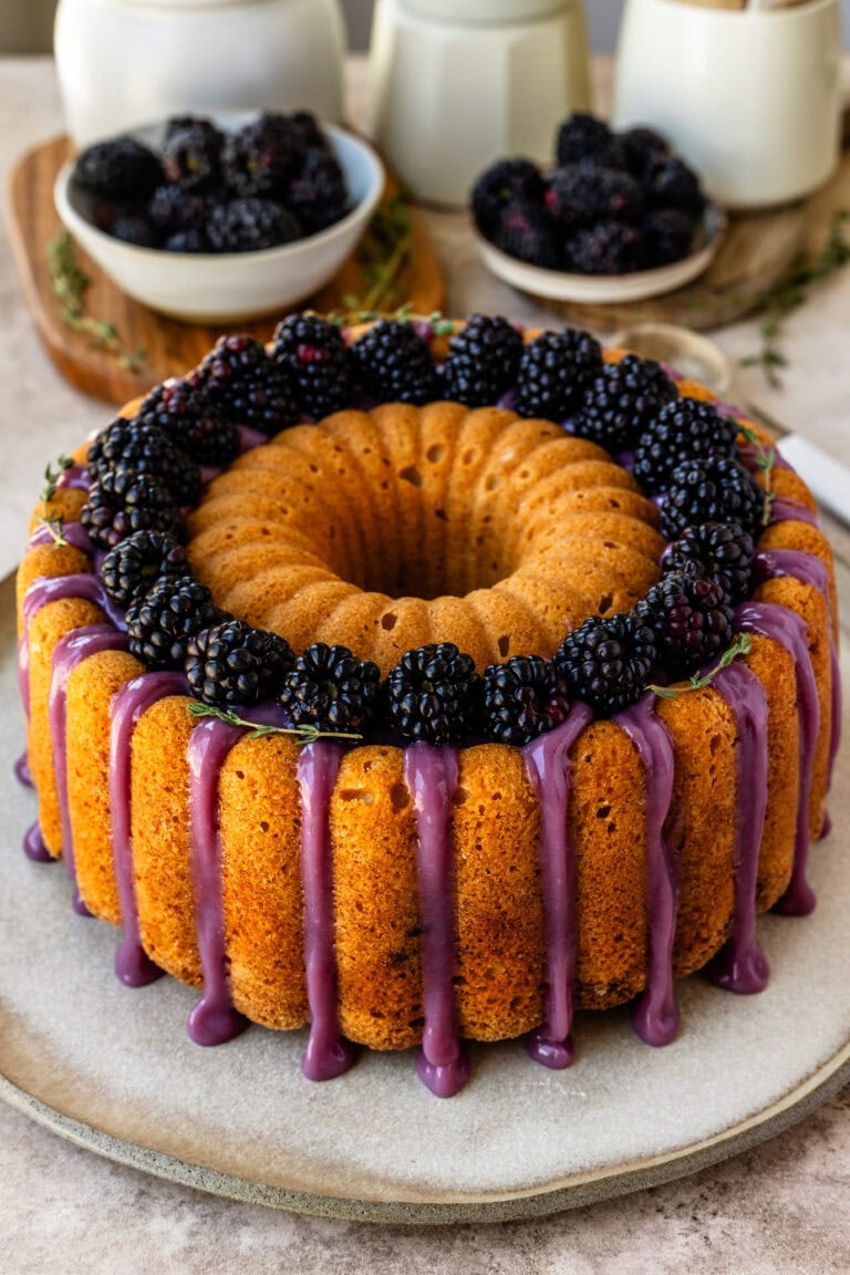 Blackberry bundt cake topped with fresh blackberries and a purple blackberry ganache dripping down the sides.