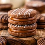 Two beautifully stacked chocolate alfajor cookies on a wooden board.