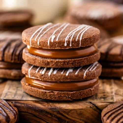 Two beautifully stacked chocolate alfajor cookies on a wooden board.