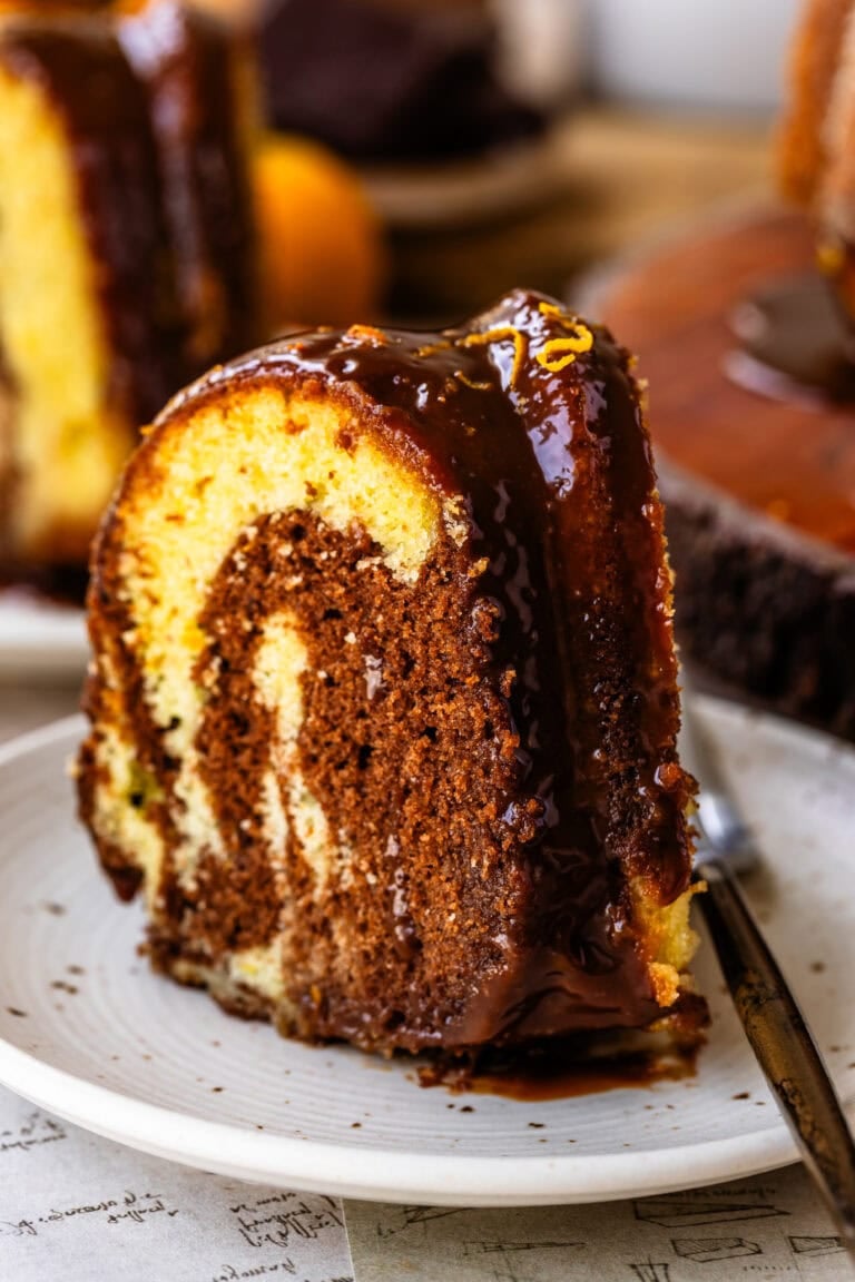 A sliced orange marble bundt cake with chocolate ganache showing the swirled chocolate and orange interior.