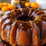 Orange marble bundt cake drizzled with chocolate ganache on a wooden serving board.