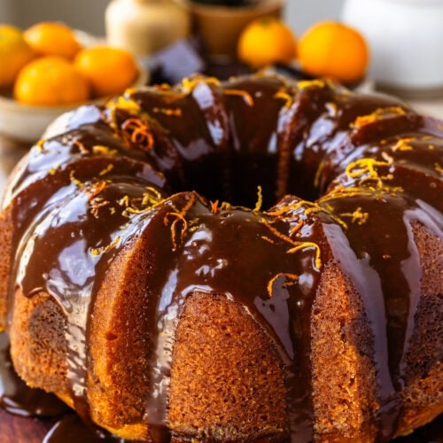 Orange marble bundt cake drizzled with chocolate ganache on a wooden serving board.
