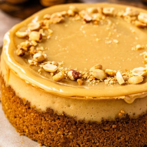 A whole peanut butter cheesecake with peanut topping and peanut butter ganache on a white plate.