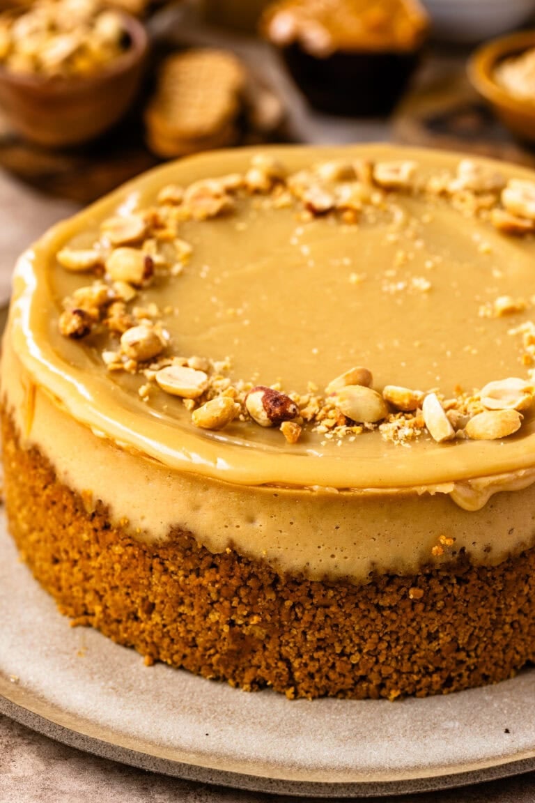 A whole peanut butter cheesecake with peanut topping and peanut butter ganache on a white plate.