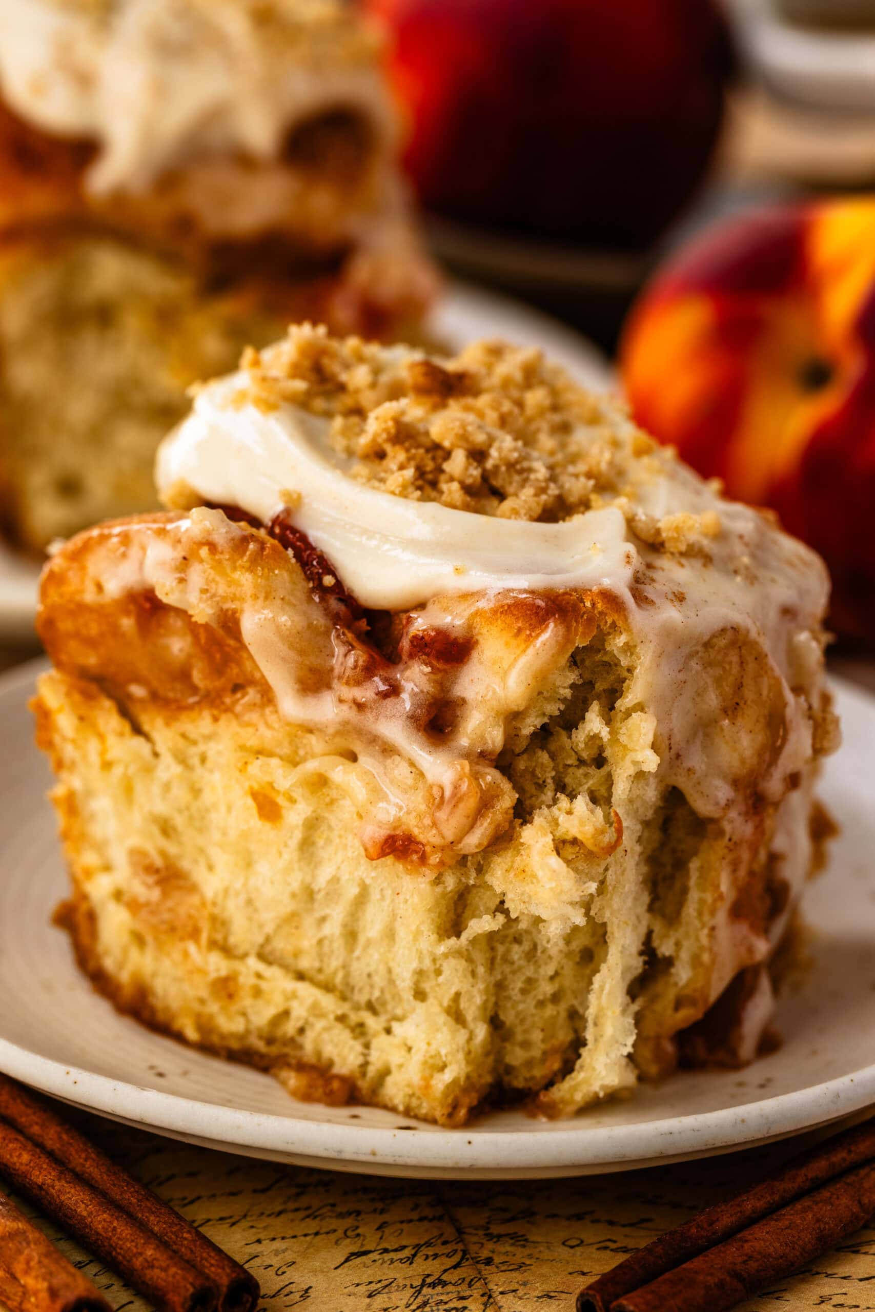 Single Peach Cobbler Cinnamon Roll on a plate with creamy cinnamon frosting and streusel topping, highlighting the tender, pillowy texture of the roll.