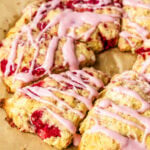Freshly baked raspberry white chocolate scones drizzled with raspberry cream cheese glaze on a parchment-lined baking sheet.