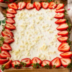 Strawberry Chantilly sheet cake topped with fluffy Chantilly frosting, fresh strawberry halves around the edges, and white chocolate curls scattered over the top.