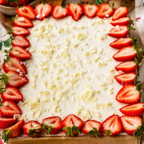 Strawberry Chantilly sheet cake topped with fluffy Chantilly frosting, fresh strawberry halves around the edges, and white chocolate curls scattered over the top.