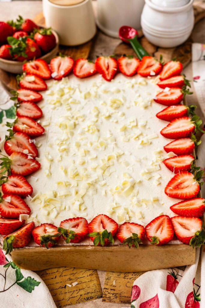 Strawberry Chantilly sheet cake topped with fluffy Chantilly frosting, fresh strawberry halves around the edges, and white chocolate curls scattered over the top.