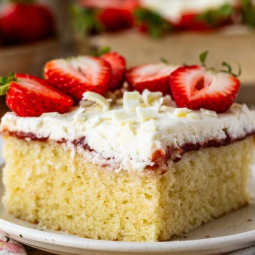 Slice of Strawberry Chantilly Sheet Cake topped with fresh strawberries, fluffy Chantilly frosting, strawberry sauce, and white chocolate curls on a dessert plate