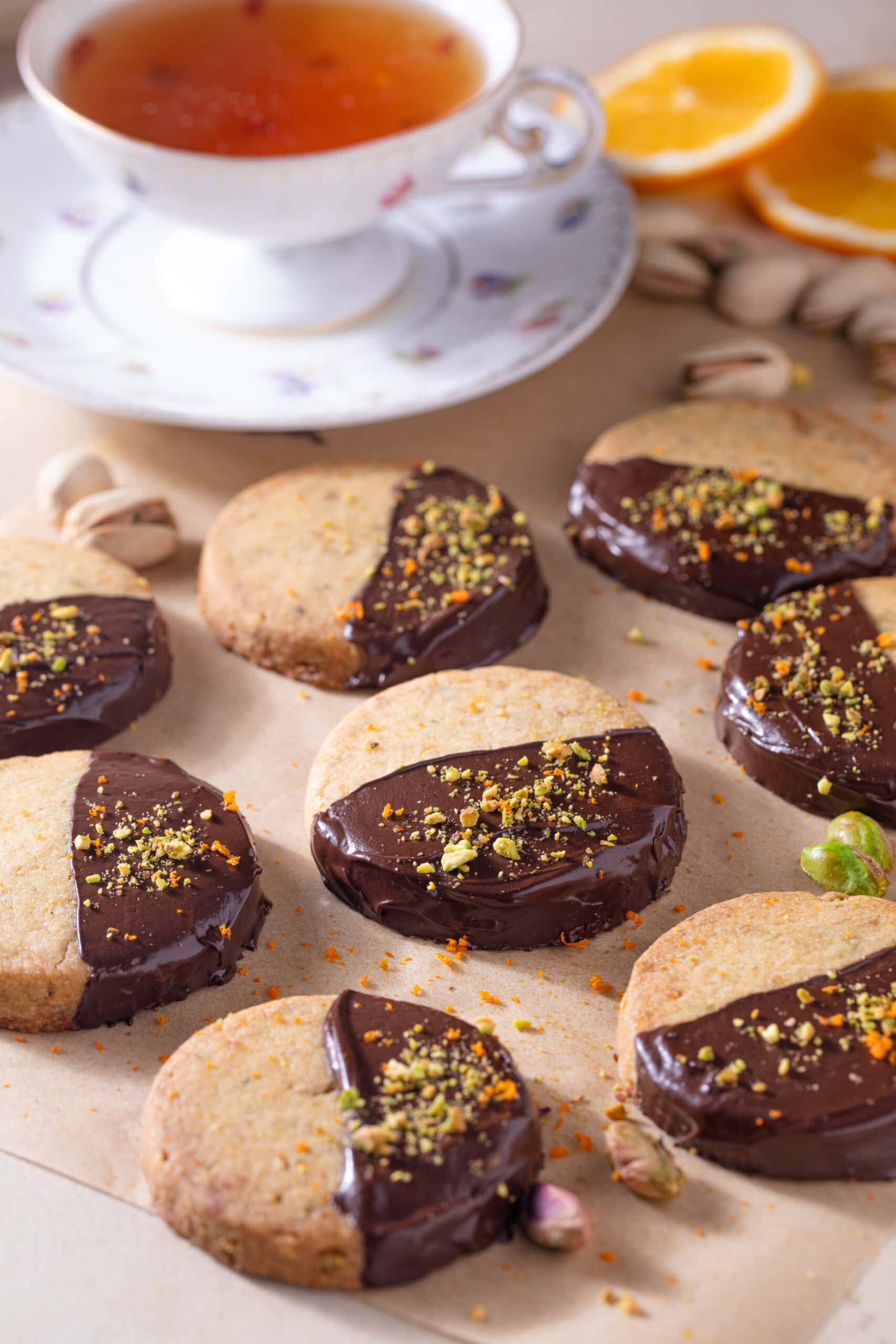 Chocolate-dipped cookies topped with crushed pistachios on a baking sheet.
