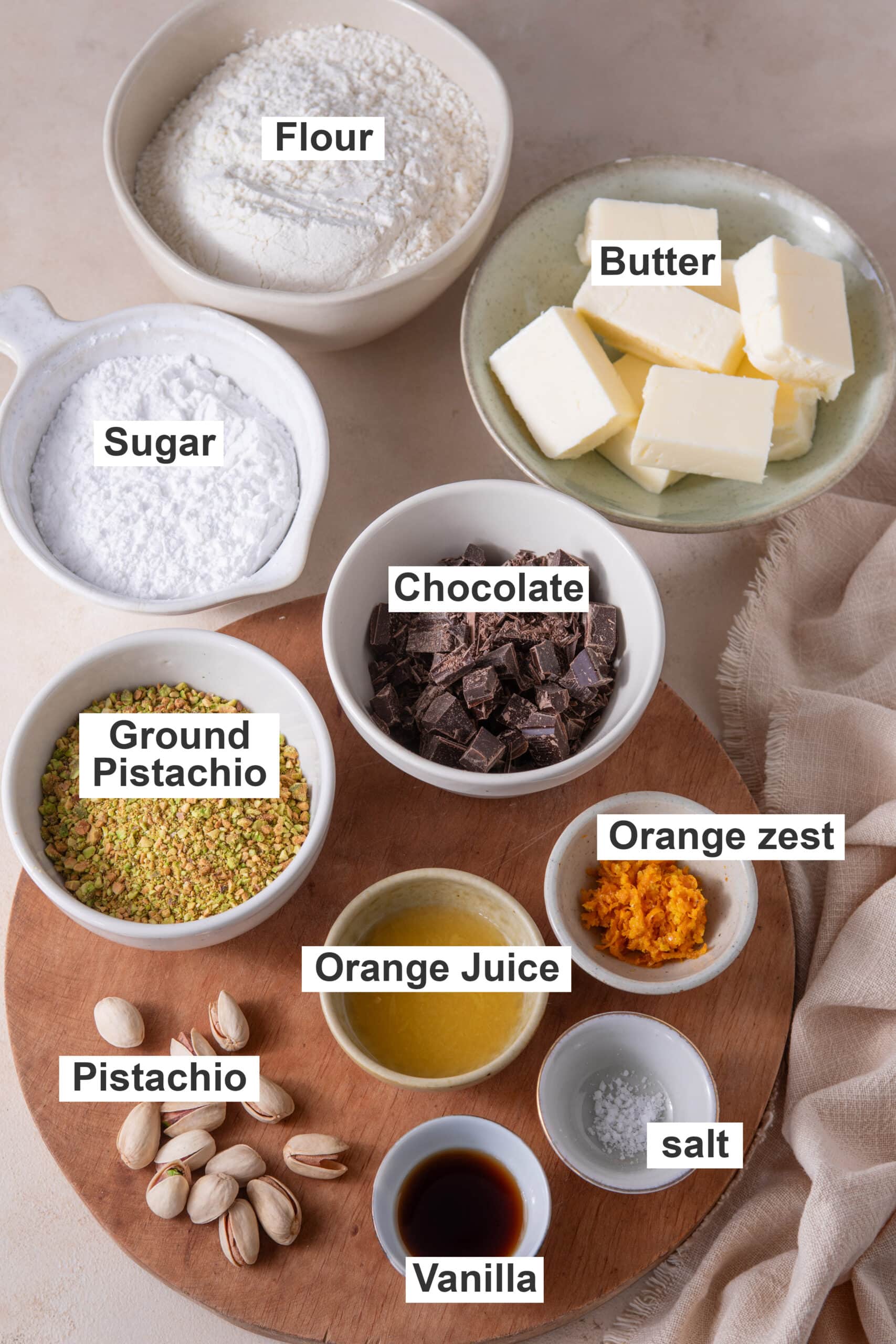 Ingredients for orange pistachio shortbread cookies including butter, pistachios, orange zest, chocolate, flour, and powdered sugar