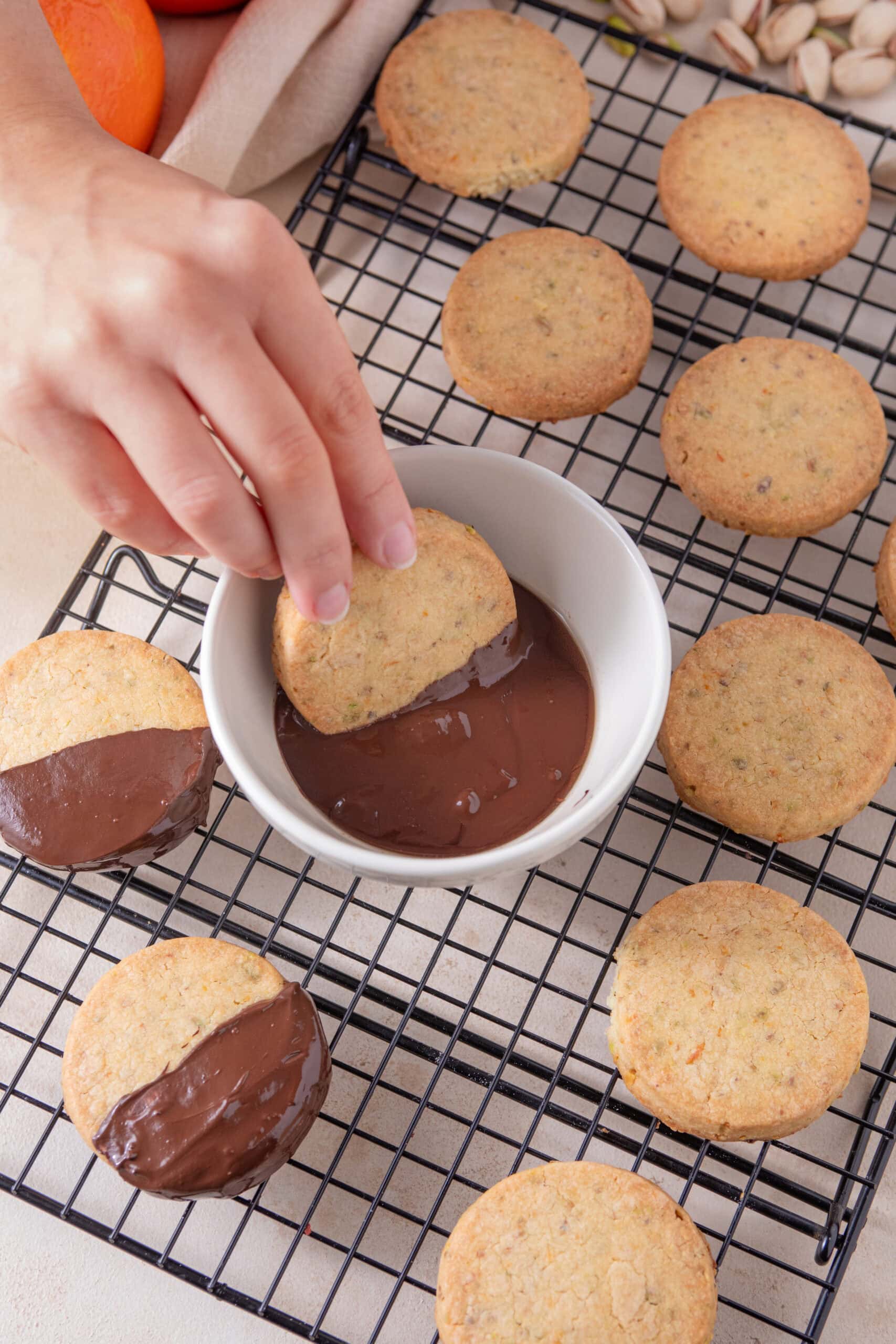 Chocolate-coated orange pistachio shortbread cookie being dipped into melted chocolate