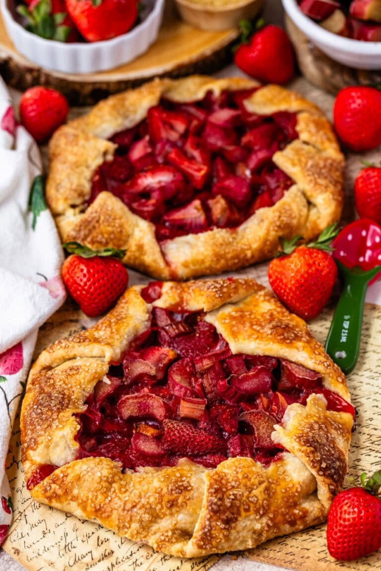 Baked strawberry rhubarb galettes with golden flaky crusts and juicy fruit filling on a serving platter.