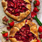 Baked strawberry rhubarb galettes with golden flaky crusts and juicy fruit filling on a serving platter.