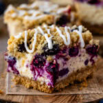 Close-up of a blueberry cheesecake bars topped with crumb streusel and a drizzle of cream cheese glaze.