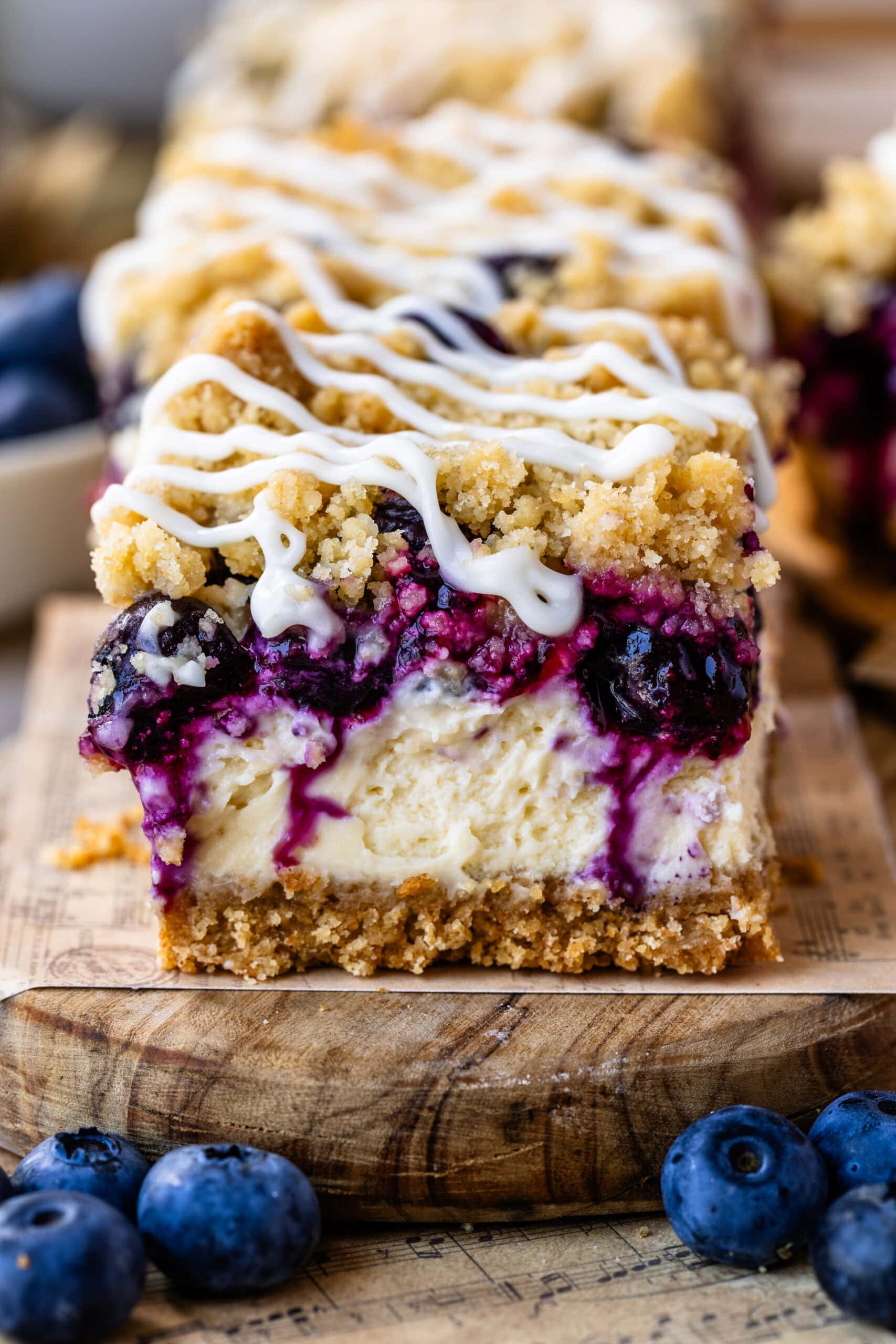 Close-up of a blueberry cheesecake bars topped with crumb streusel and a drizzle of cream cheese glaze.