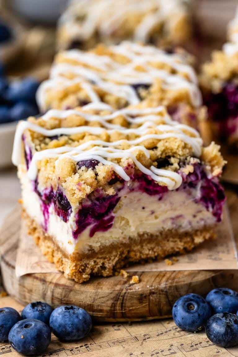 Close-up of a blueberry cheesecake bars topped with crumb streusel and a drizzle of cream cheese glaze.
