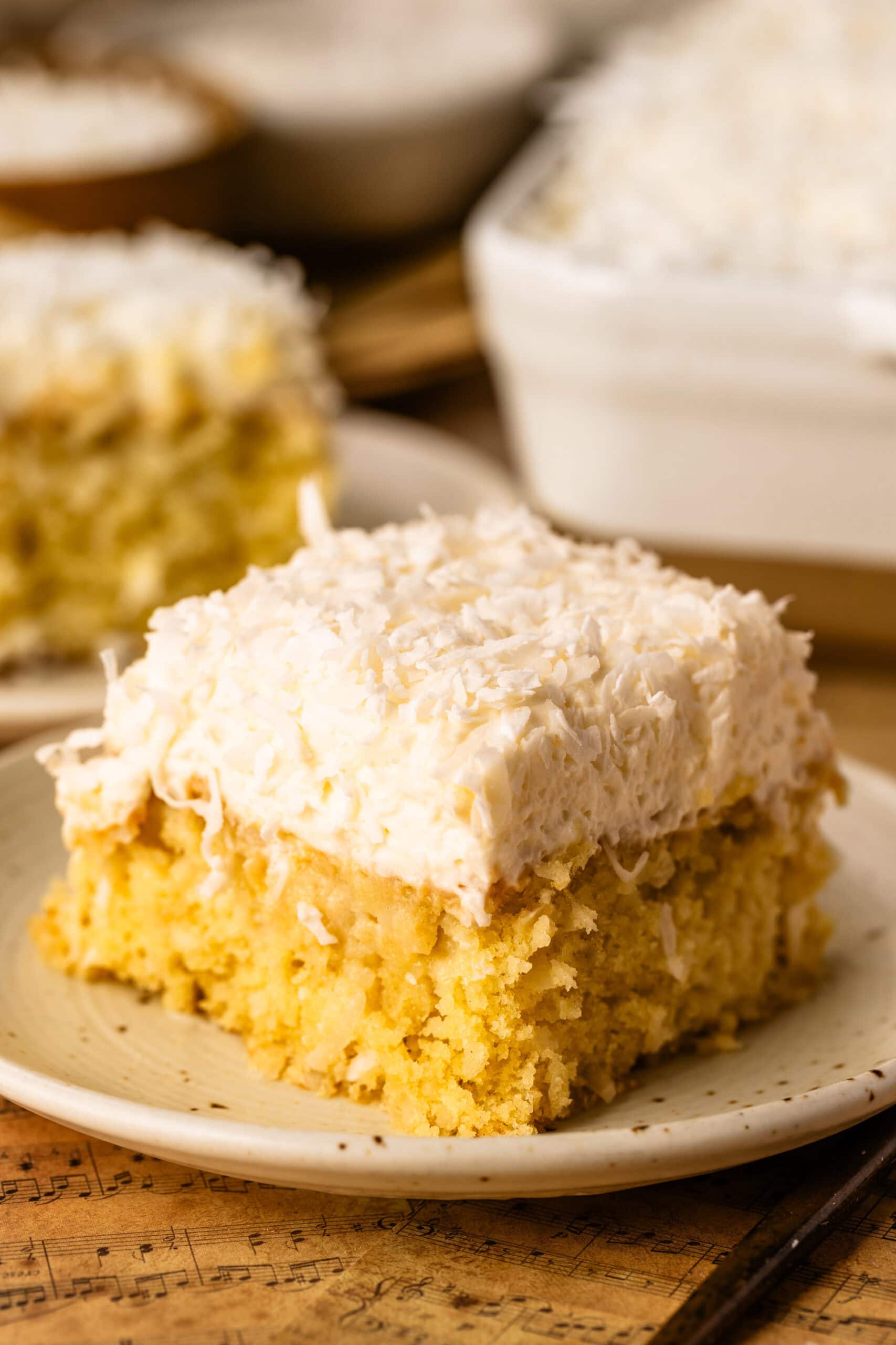 A single slice of delicate coconut cake that has been soaked with a coconut milk soak, topped with coconut cloud frosting and shredded coconut.