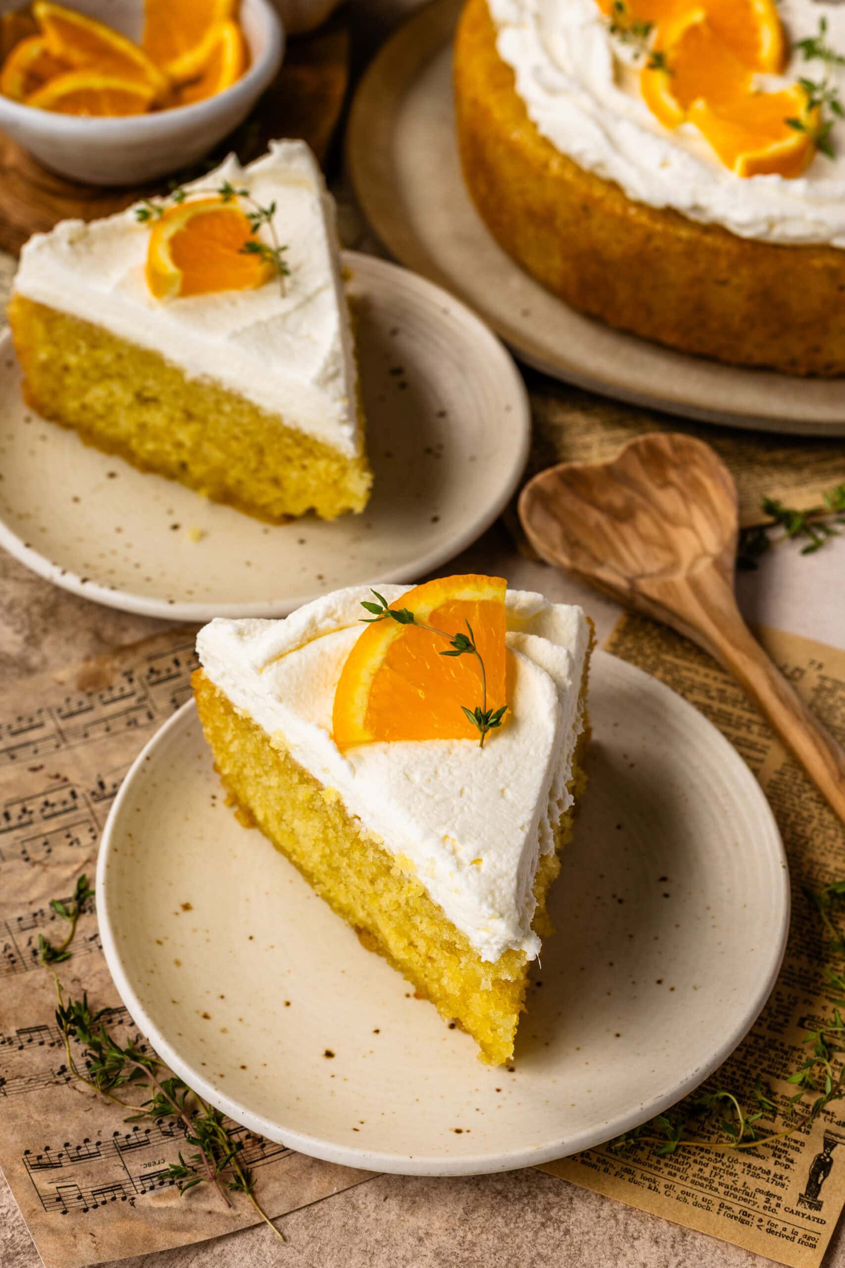 A slice of olive oil cake topped with mascarpone whipped cream, orange slices, and fresh thyme.
