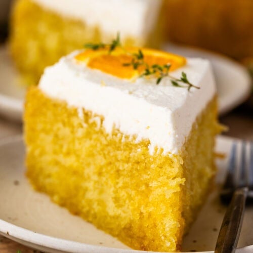 A slice of olive oil cake topped with mascarpone whipped cream, orange slices, and fresh thyme.