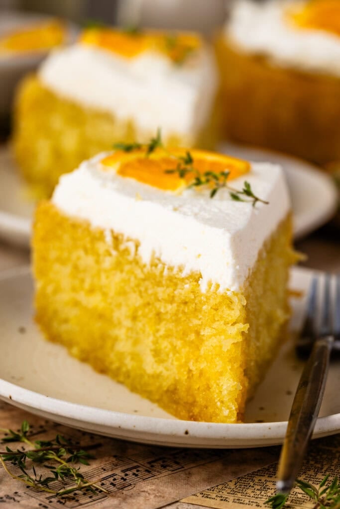A slice of olive oil cake topped with mascarpone whipped cream, orange slices, and fresh thyme.