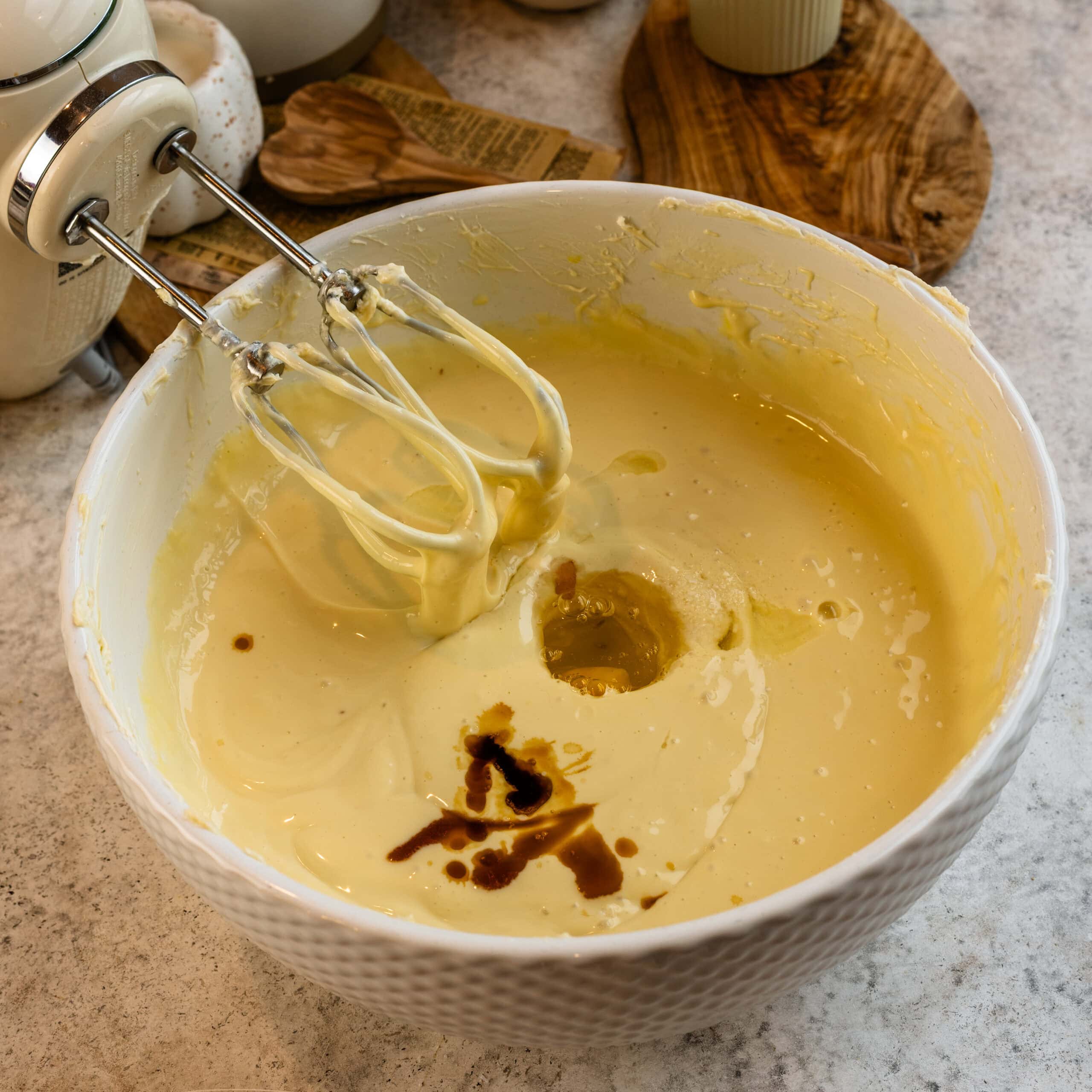 Cream cheese cheesecake filling being mixed with an electric mixer. An egg and vanilla has just been added.