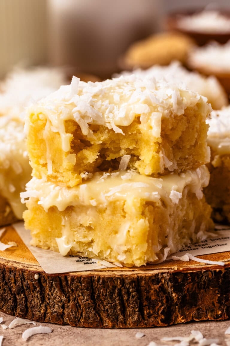 Stack of Coconut Blondies with coconut white chocolate ganache and shredded coconut on top.