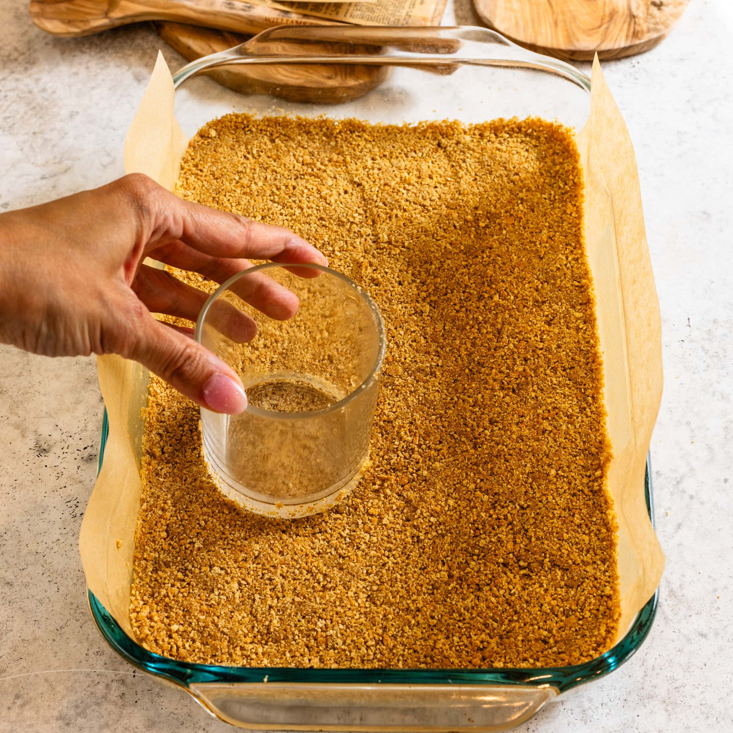 Using a glass to press the graham cracker crust into an even layer.