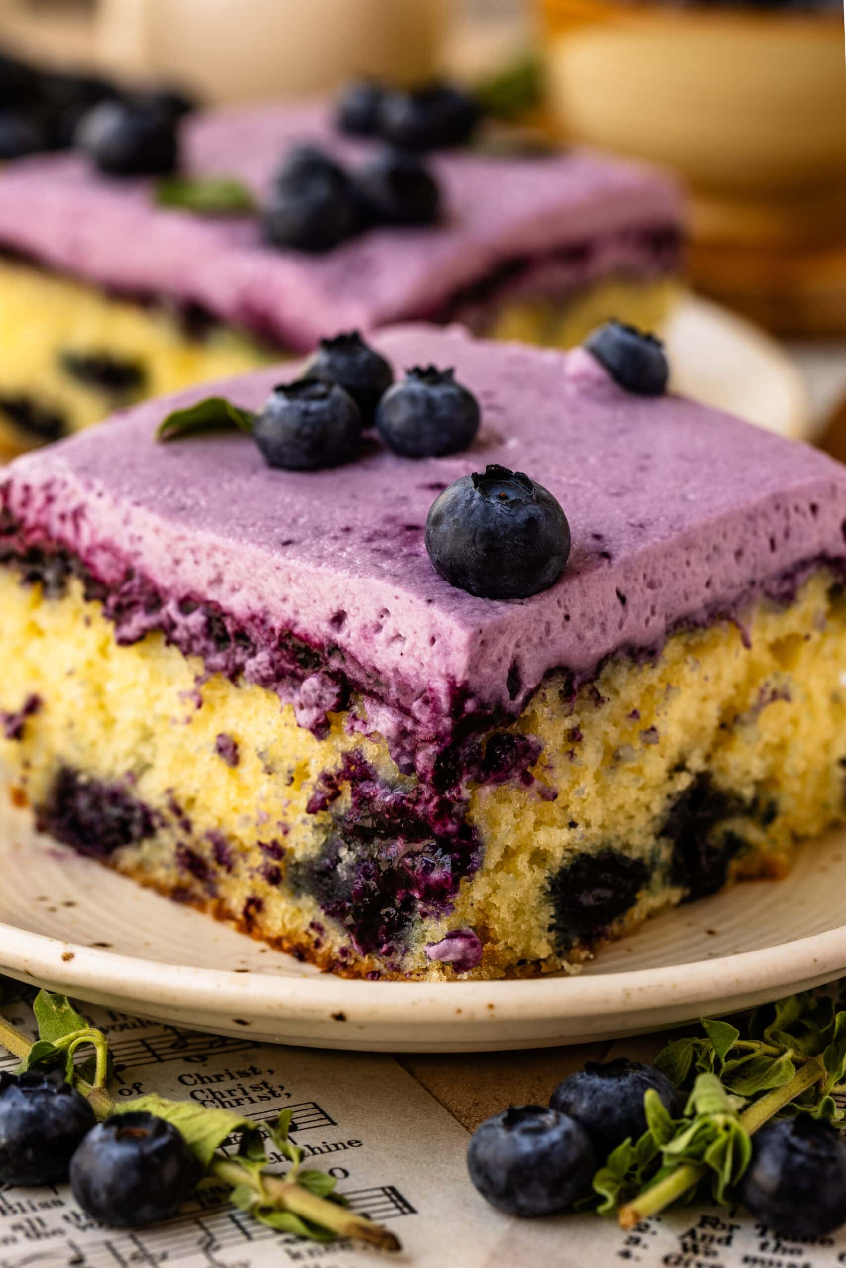 Slice of Blueberry Chantilly Sheet Cake topped with fluffy blueberry frosting and fresh blueberries.