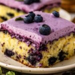 Slice of Blueberry Chantilly Sheet Cake topped with fluffy blueberry frosting and fresh blueberries.